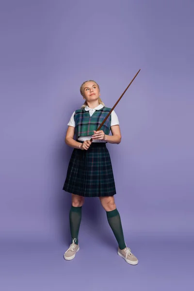 Повна довжина студента в уніформі тримає вказівник на фіолетовому фоні — стокове фото