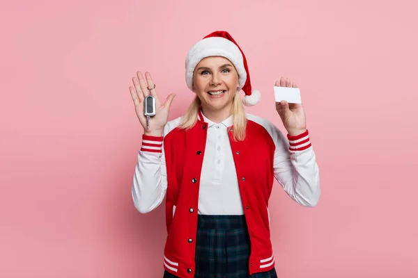 Cheerful blonde woman in santa hat holding driving license and car key on pink background — Foto stock