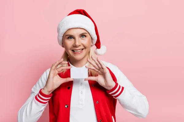 Cheerful woman in santa hat holding empty driving license isolated on pink — стоковое фото