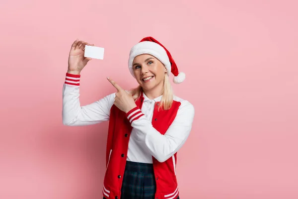 Cheerful woman in santa hat pointing at empty driving license on pink background - foto de stock
