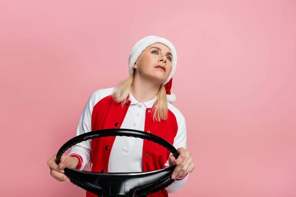 Blonde woman in santa hat holding steering wheel isolated on pink — Stock Photo