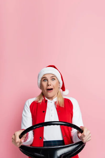 Scared woman in santa hat holding steering wheel isolated on pink — Fotografia de Stock