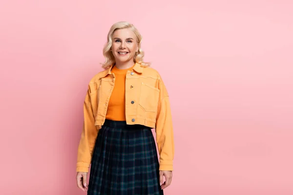 Positive woman in orange jacket looking at camera isolated on pink — стоковое фото