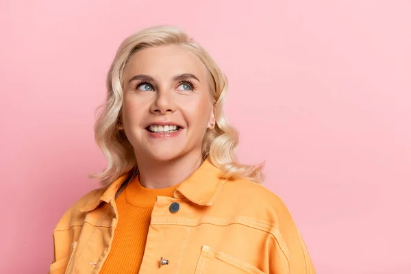 Portrait of smiling blonde woman looking up isolated on pink — стоковое фото