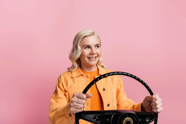 Blonde woman holding steering wheel and looking away isolated on pink — Stock Photo