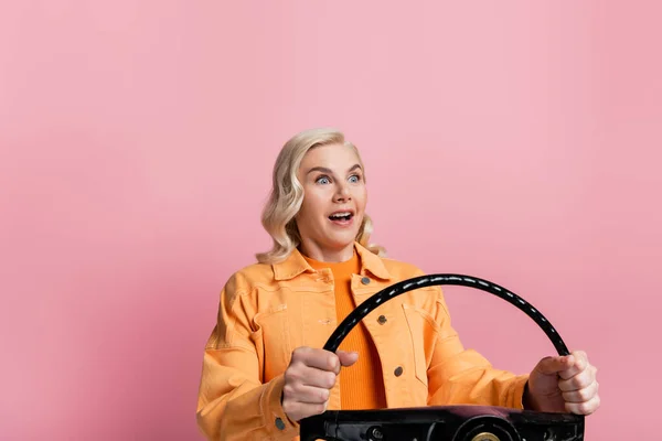 Шокований водій блондинки тримає кермо ізольовано на рожевому — стокове фото