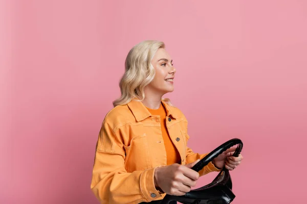 Smiling driver holding steering wheel on driving course isolated on pink — стоковое фото