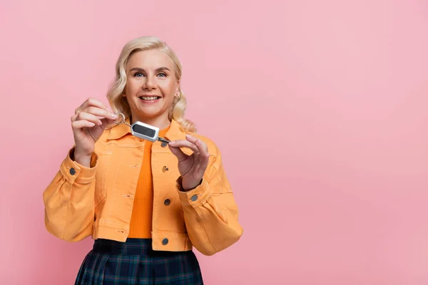 Smiling blonde driver holding car key isolated on pink — Photo de stock