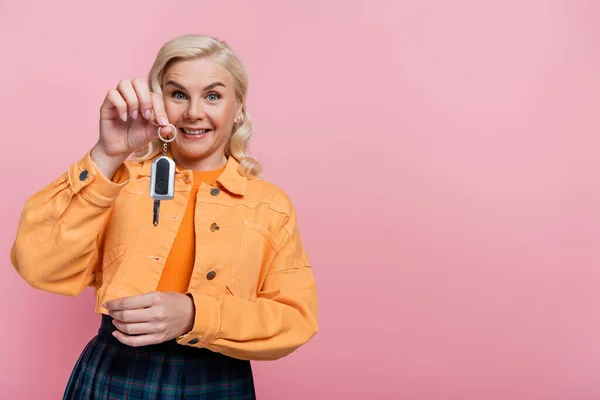 Smiling blonde woman holding car key isolated on pink with copy space — стоковое фото