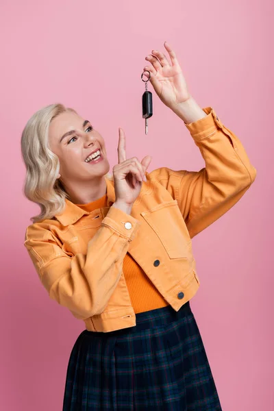 Positive blonde woman pointing at car key isolated on pink — Stock Photo