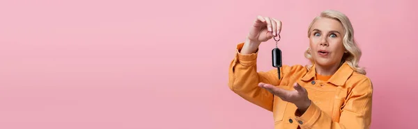 Amazed blonde woman pointing at car key isolated on pink, banner - foto de stock