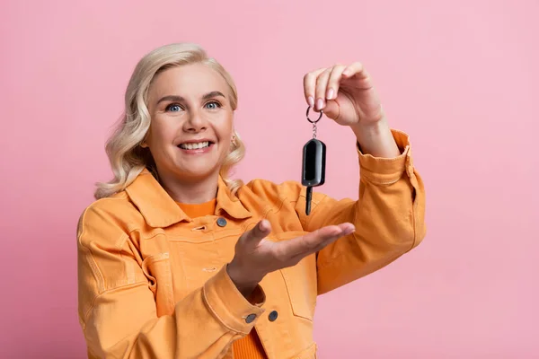 Positive blonde woman holding car key isolated on pink — Stock Photo