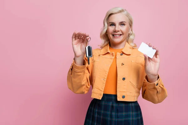 Happy blonde driver in jacket holding empty driving license and car key isolated on pink - foto de stock