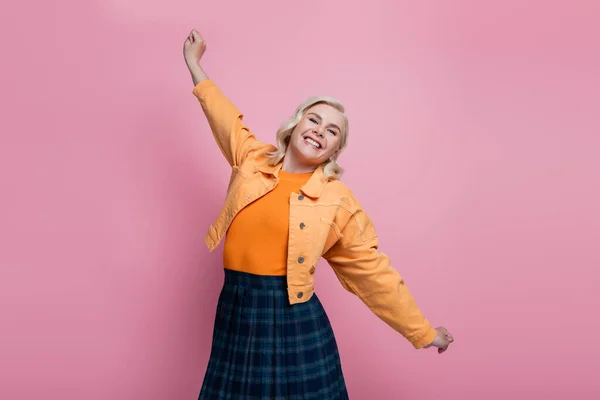 Positive woman in orange jacket stretching isolated on pink — Fotografia de Stock