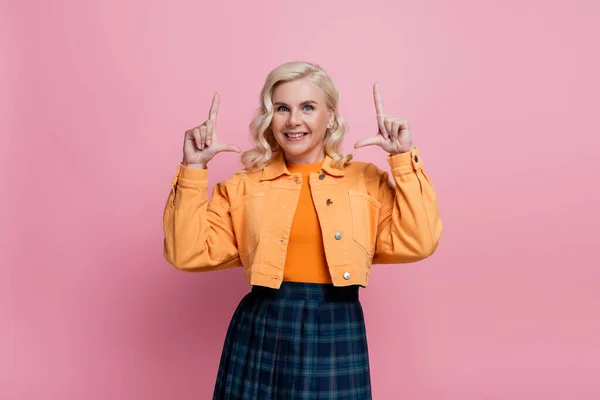 Smiling blonde woman looking at camera and pointing with fingers isolated on pink — стоковое фото