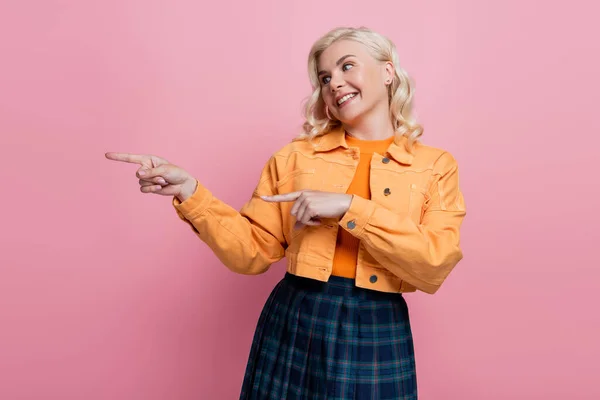 Smiling woman pointing with fingers and looking away isolated on pink — стоковое фото