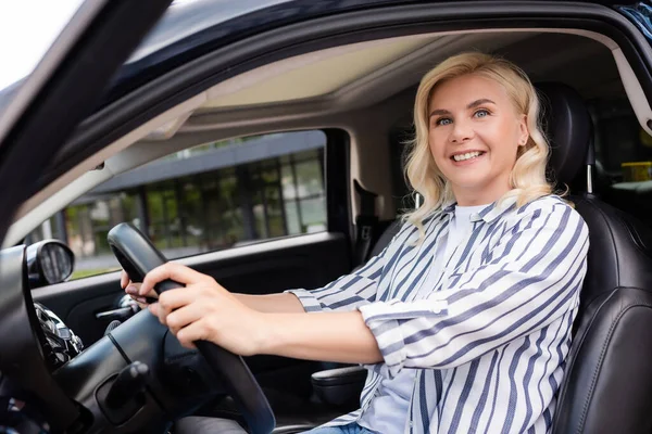 Cheerful woman looking at camera while sitting in car during driving course — стоковое фото