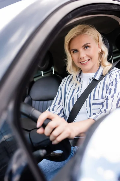 Positive blonde woman looking at camera in auto during driving courses - foto de stock