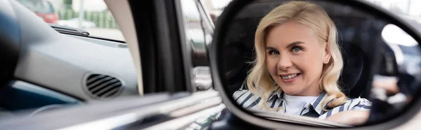 Cheerful blonde woman reflecting in blurred mirror of auto, banner — стоковое фото