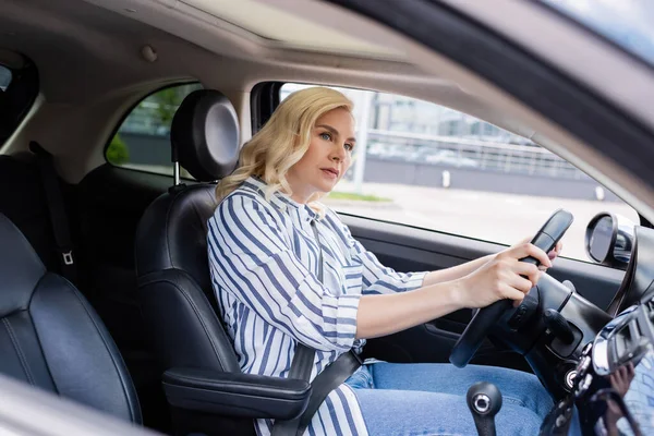 Blonde driver looking away while driving car during course in car — Photo de stock