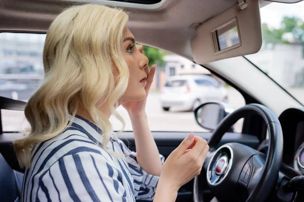 Side view of blonde woman looking at mirror in car — стоковое фото