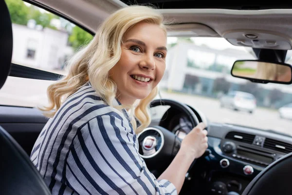 Позитивна блондинка дивиться на камеру під час керування автомобілем — стокове фото