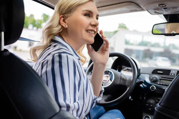 Smiling woman talking on smartphone on driving seat in car — стоковое фото