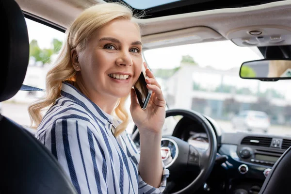 Cheerful driver looking at camera while talking on smartphone in car - foto de stock