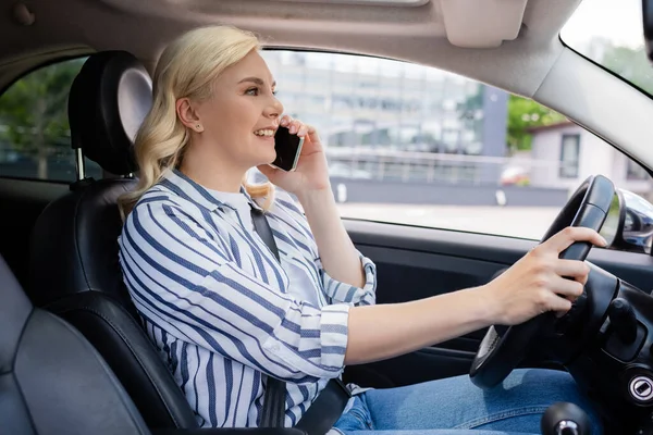 Side view of positive blonde woman talking on cellphone in car — стоковое фото