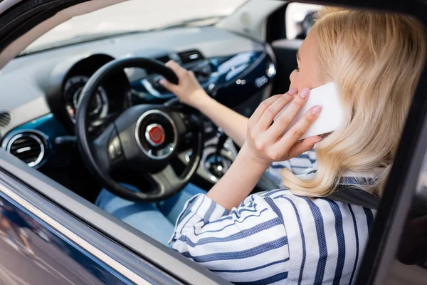 Blonde woman talking on smartphone while driving blurred car — Stock Photo