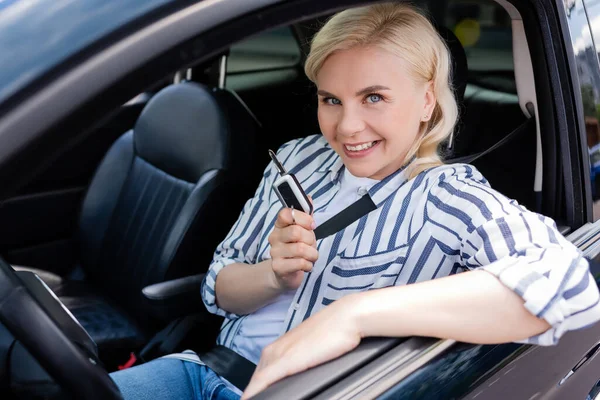 Positive driver holding key and looking at camera in car — Stock Photo