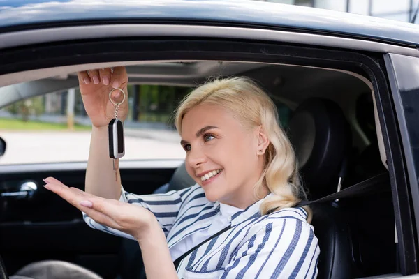 Blonde driver looking at key while sitting in auto — Photo de stock