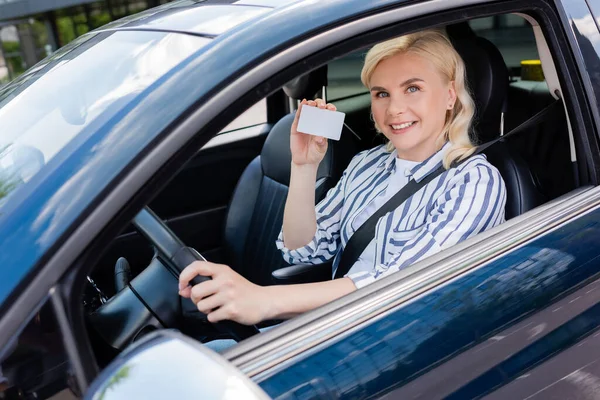 Smiling blonde woman holding driver license on driver seat in car — Stock Photo