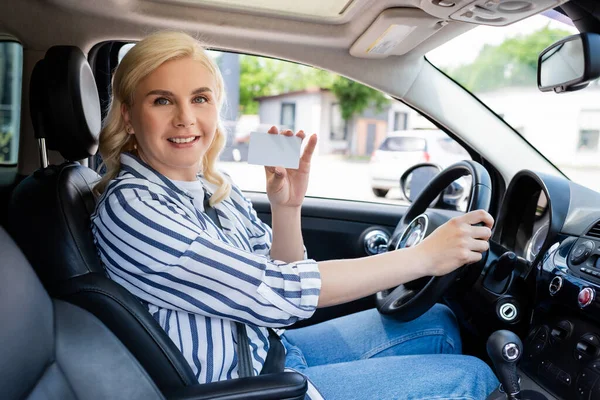 Positive blonde driver holding license in auto — Foto stock