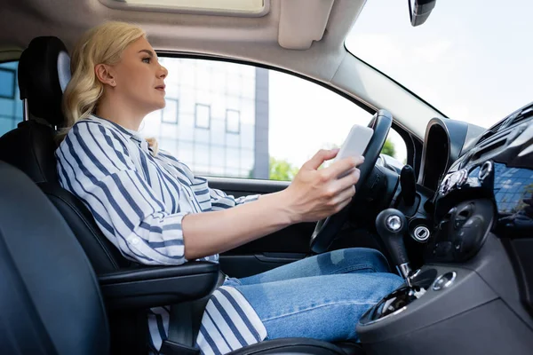 Side view of woman using smartphone and driving car — Stock Photo