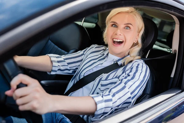 Amazed blonde woman looking at camera while driving car - foto de stock