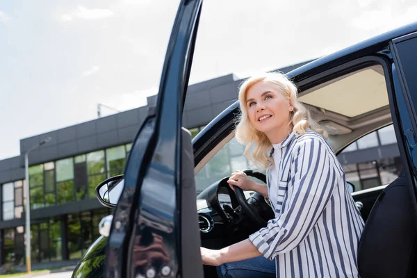 Smiling woman opening door of car and looking away outdoors — стоковое фото