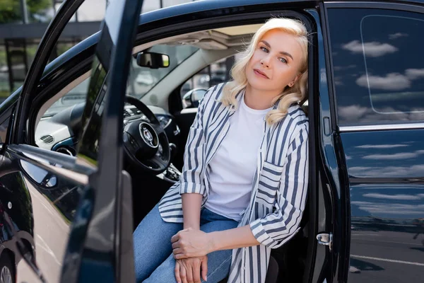 Tired blonde driver sitting in car with open door at daytime - foto de stock
