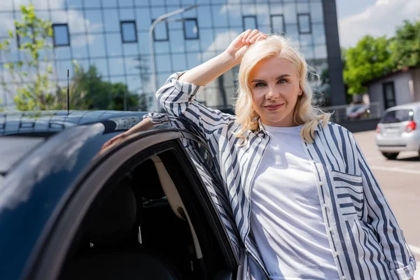 Smiling woman looking at camera near car on urban street — Stockfoto