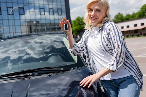 Happy owner holding key near car on urban street — Stockfoto