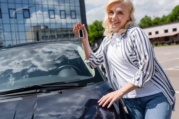 Happy owner holding key near car on urban street — Stock Photo