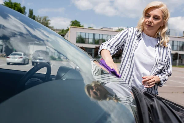 Driver cleaning windshield of car on urban street — стоковое фото