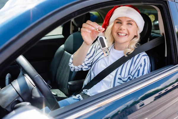 Cheerful driver in santa hat holding key in auto — стоковое фото