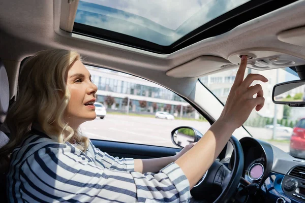 Blonde driver in casual clothes pushing button in car — Fotografia de Stock