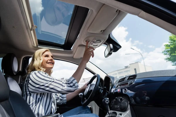 Positive blonde woman pushing button and looking at top of car — стоковое фото