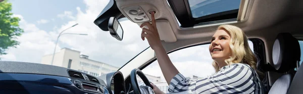 Cheerful driver pushing button and looking at window on top of car, banner - foto de stock