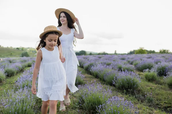 Happy woman looking away while walking with daughter in lavender meadow — Photo de stock