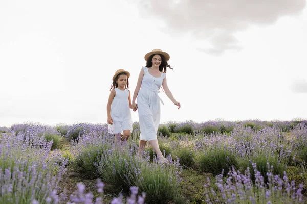 Woman and girl in white dresses holding hands while walking in lavender field — Foto stock