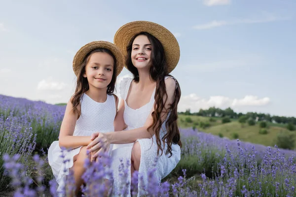 Cheerful mom and daughter sitting in lavender field and looking at camera — Stock Photo