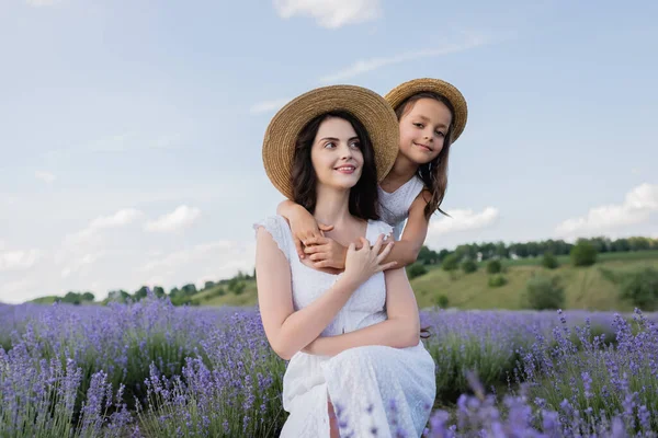 Happy kid embracing mom and looking at camera in lavender field - foto de stock